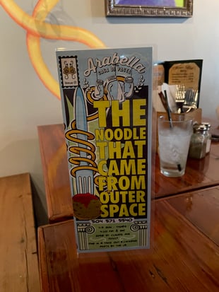 The front cover of Arabella's comic-book themed menu. In large yellow text are the words THE NOODLE THAT CAME FROM OUTER SPACE, and there is a fork skewering a meatball.